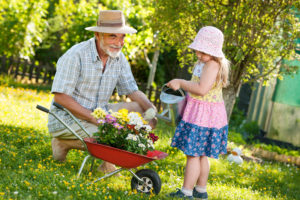 Train your body for adaptability. | Picture of grandfather kneeling as little girl waters flowers. | Senior Fitness
